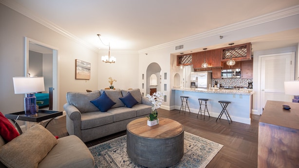 A modern living room with a grey sofa, a round coffee table, and a kitchen area with a bar counter. - Pool-side 2 Bedroom Viera condo! (Henderson)