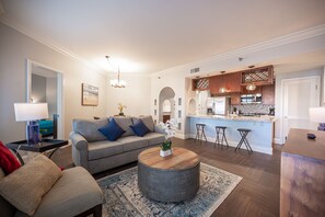 Een moderne woonkamer met een grijze bank, een ronde salontafel en een keuken met een bar.