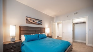 A bedroom with a large bed, two bedside tables with lamps, a wooden headboard, a painting on the wall, and a closet with a door. - Pool-side 2 Bedroom Viera condo! (Henderson)