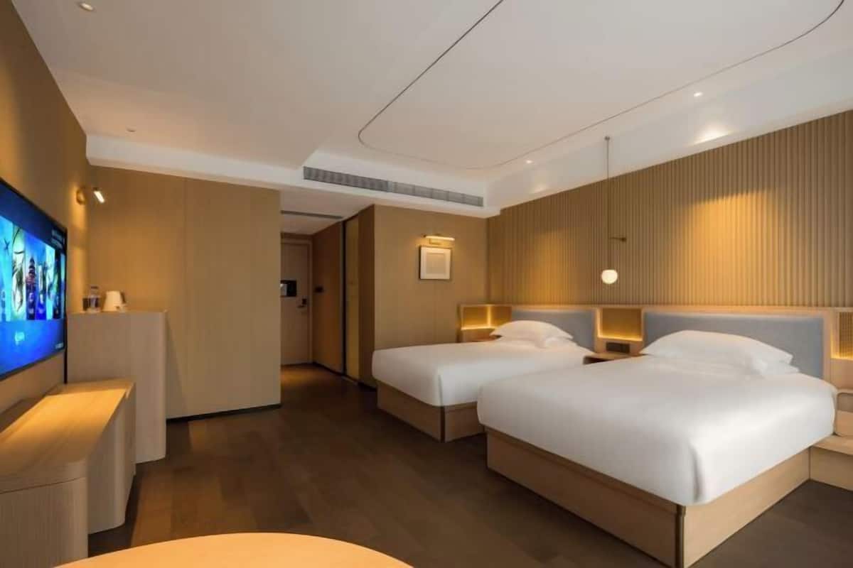 Une chambre d’hôtel avec deux lits, une télévision et un bureau avec une lampe.