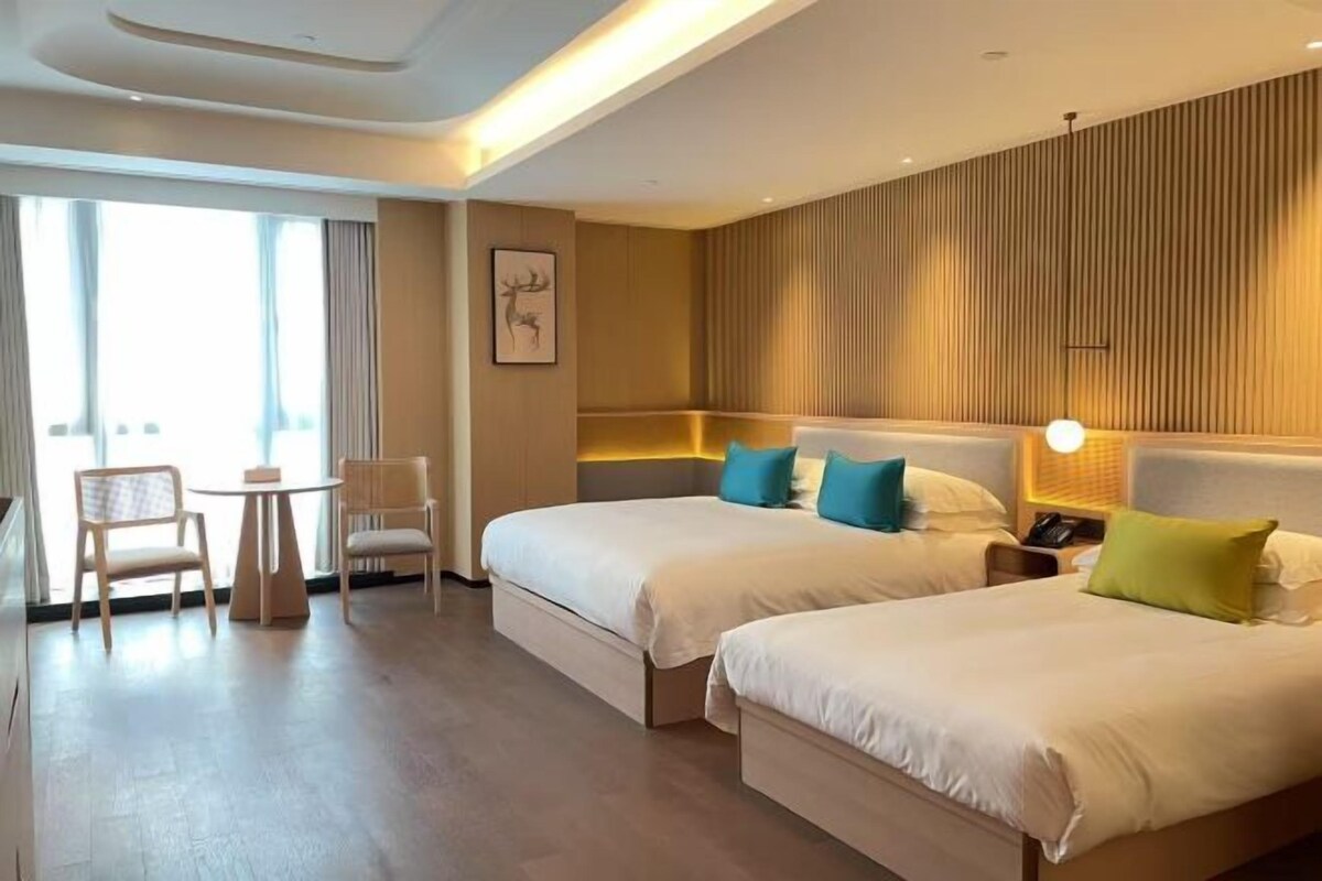 A hotel room with two beds, a small table, chairs, and a large window.