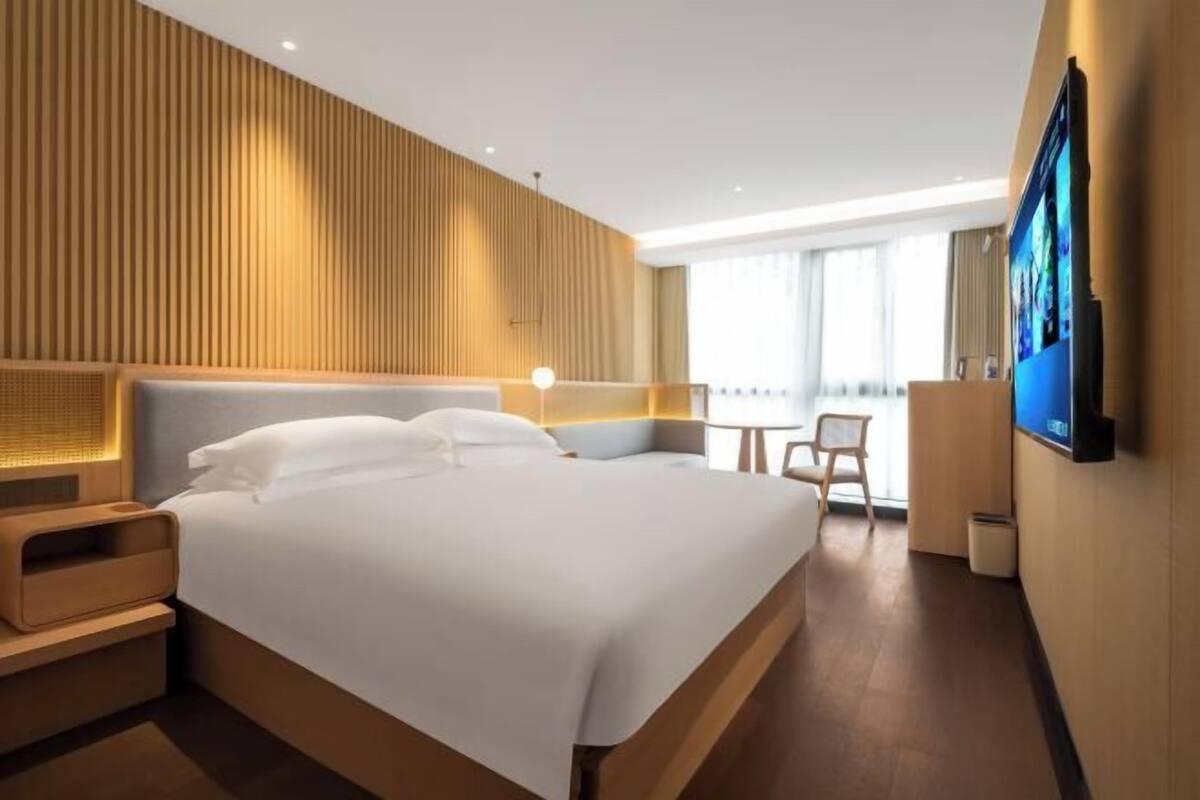 Une chambre d’hôtel moderne avec un grand lit, des tables de chevet, une télévision et un bureau avec une chaise.