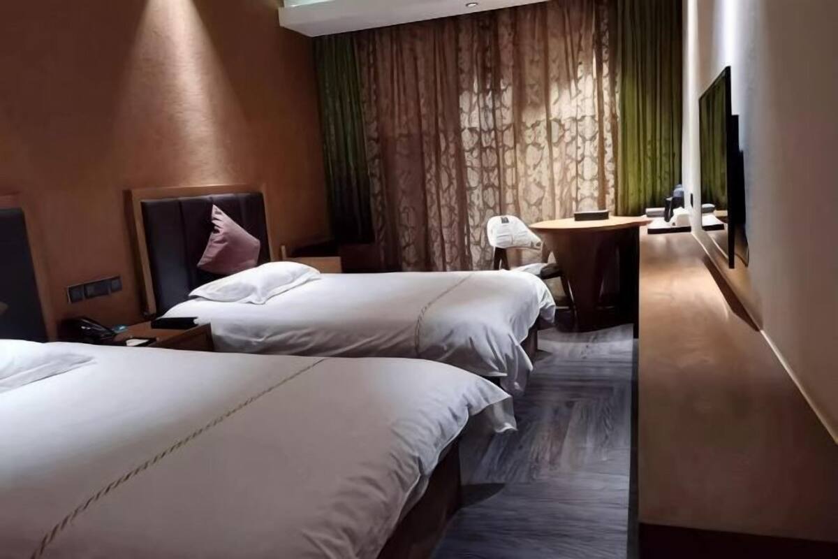 Une chambre d’hôtel avec deux lits, un bureau, une chaise, une télévision et une fenêtre avec des rideaux.