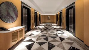 A modern hotel lobby with a geometric patterned floor, a reception desk, and elevators. - Hangzhou Chengbei Relax Hotel (Hangzhou)