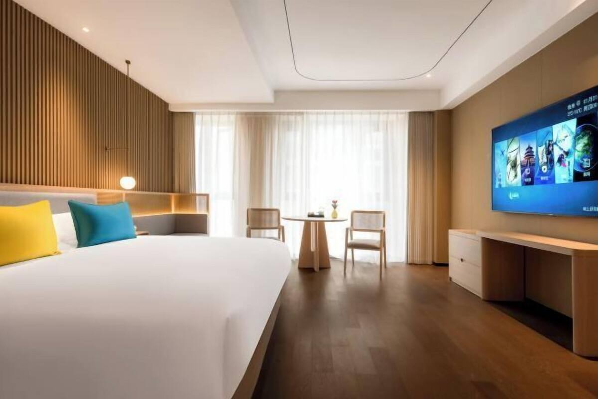 Une chambre d’hôtel avec un grand lit, un bureau, une télévision et une fenêtre avec des rideaux.