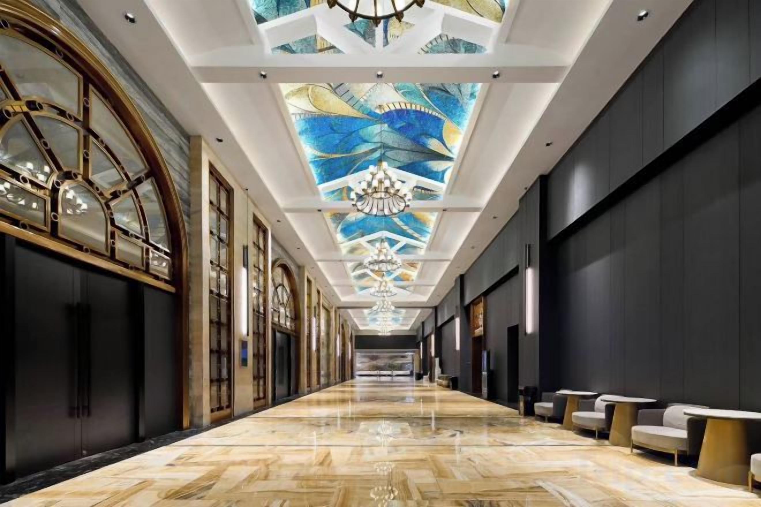 Un largo pasillo pulido con techo decorado con un diseño geométrico y candelabros.