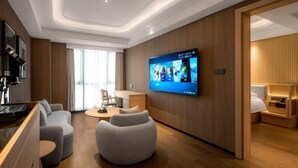 A modern hotel room with a flat-screen TV, a sofa, a coffee table, and a wooden accent wall. - Hangzhou Chengbei Relax Hotel (Hangzhou)