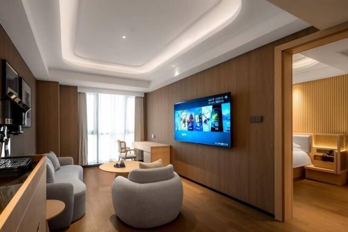 Une chambre d’hôtel moderne dotée d’une télévision à écran plat, d’un canapé, d’une table basse et d’un mur décoratif en bois.