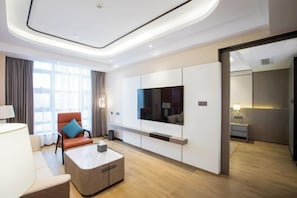 A modern hotel room with a large flat-screen TV mounted on the wall, a comfortable seating area with a sofa and armchair, and a wooden coffee table. - Hangzhou Chengbei Relax Hotel (Hangzhou)