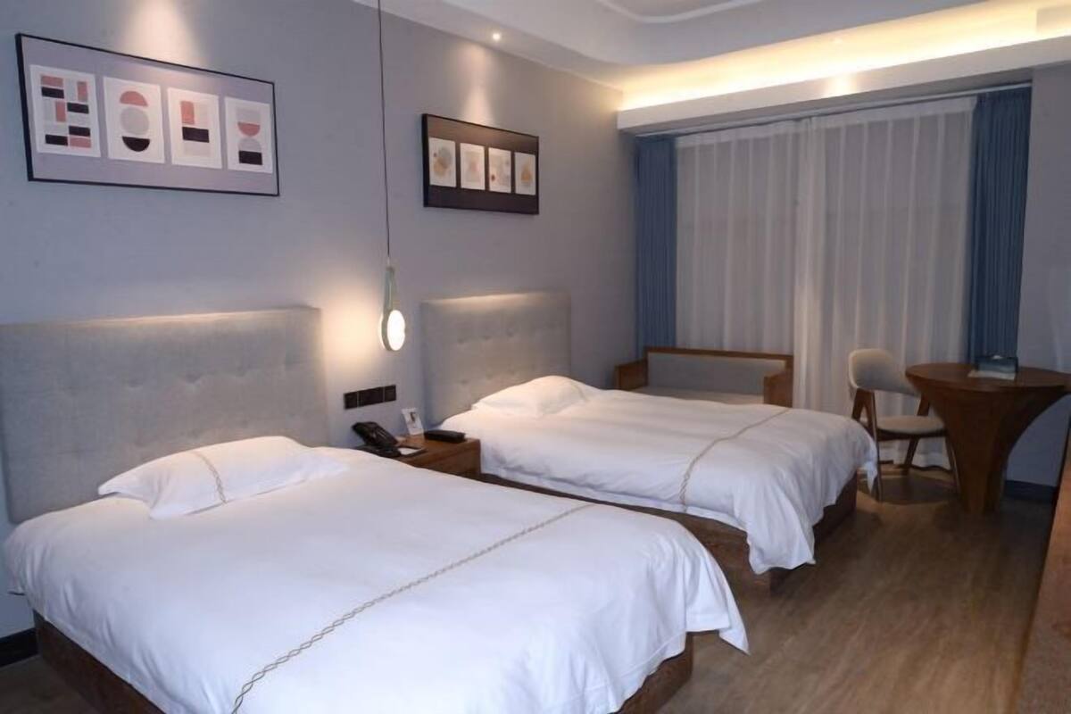 Une chambre d’hôtel avec deux lits, un bureau, une chaise et des œuvres d’art accrochées aux murs.