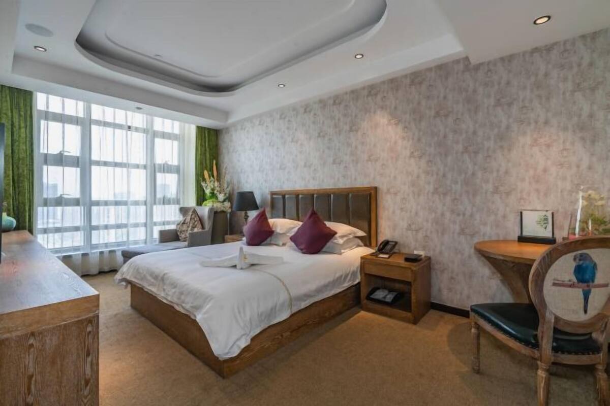 Une chambre d’hôtel avec un grand lit, un bureau, une chaise et une fenêtre avec des rideaux.
