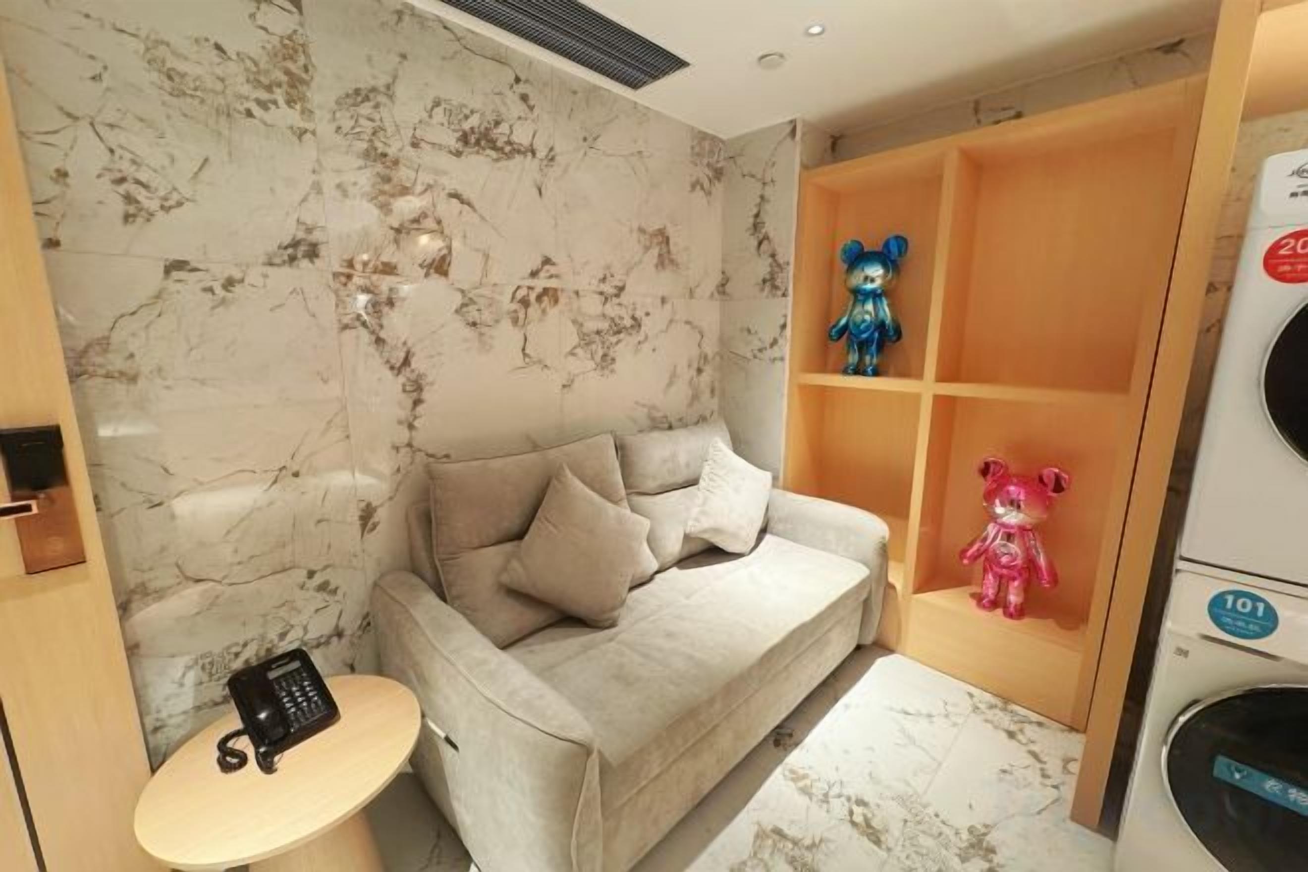 A room with a marble wall, a sofa, a small table with a phone, and a laundry machine.