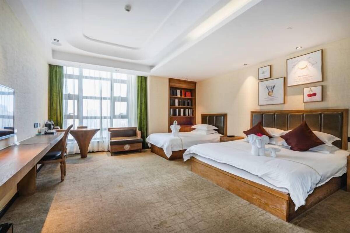 Une chambre d’hôtel avec deux lits, un bureau, une bibliothèque et une grande fenêtre.