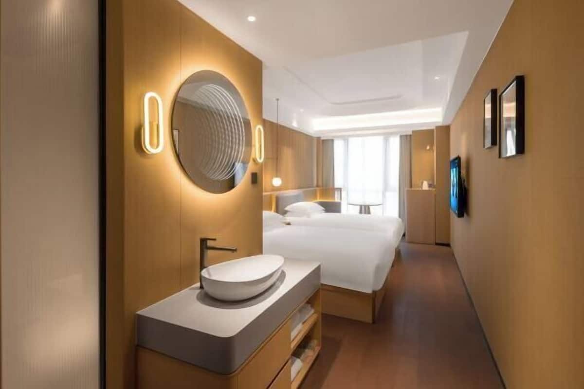 Une chambre d’hôtel moderne dotée d’un grand lit, d’un miroir rond, d’un lavabo intégré et d’un téléviseur à écran plat fixé au mur.