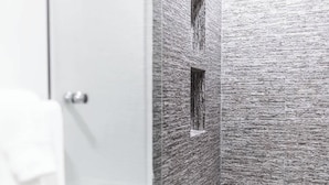 Un bany amb una cabina de dutxa de vidre, un terra emblat i una paret amb relleu.