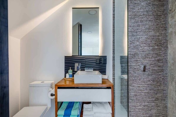 Et moderne badeværelse med et hvidt toilet, en trækommode med vask og et spejl.