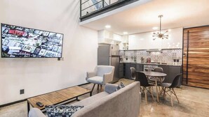 A modern living room with a sofa, chairs, and a coffee table. A large flat-screen TV is mounted on the wall. - Loft 202 (Puerto Vallarta)