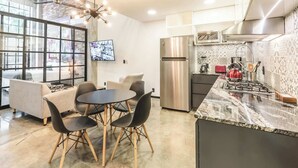 A modern kitchen with a stainless steel refrigerator, a gas stove, and a marble countertop. There is a dining area with a round table and chairs. - Loft 302 Summary:<br>We (Puerto Vallarta)
