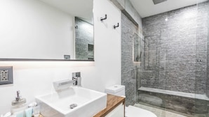 A modern bathroom with a white sink, a wooden vanity, a toilet, and a shower with a textured wall. - Room 102 (Puerto Vallarta)