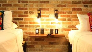 A room with two beds, a brick wall, and a wooden shelf with electrical outlets. - Room 102 (Puerto Vallarta)