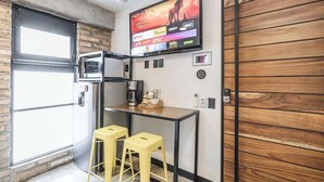 A compact kitchen with a built-in oven, a coffee machine, and a TV mounted on the wall displaying various streaming services. - Room 101 (Puerto Vallarta)
