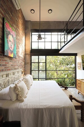 Ein Schlafzimmer mit einem großen Bett, einer Ziegelwand, einem großen Fenster und einer Treppe.