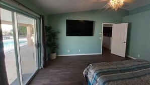 Un dormitorio con una cama grande, ventilador de techo, televisión y puerta corrediza de cristal que da a un balcón.