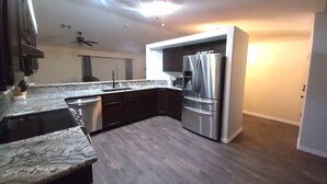 Una cocina moderna con suelo de madera oscura, electrodomésticos de acero inoxidable y encimera de granito.