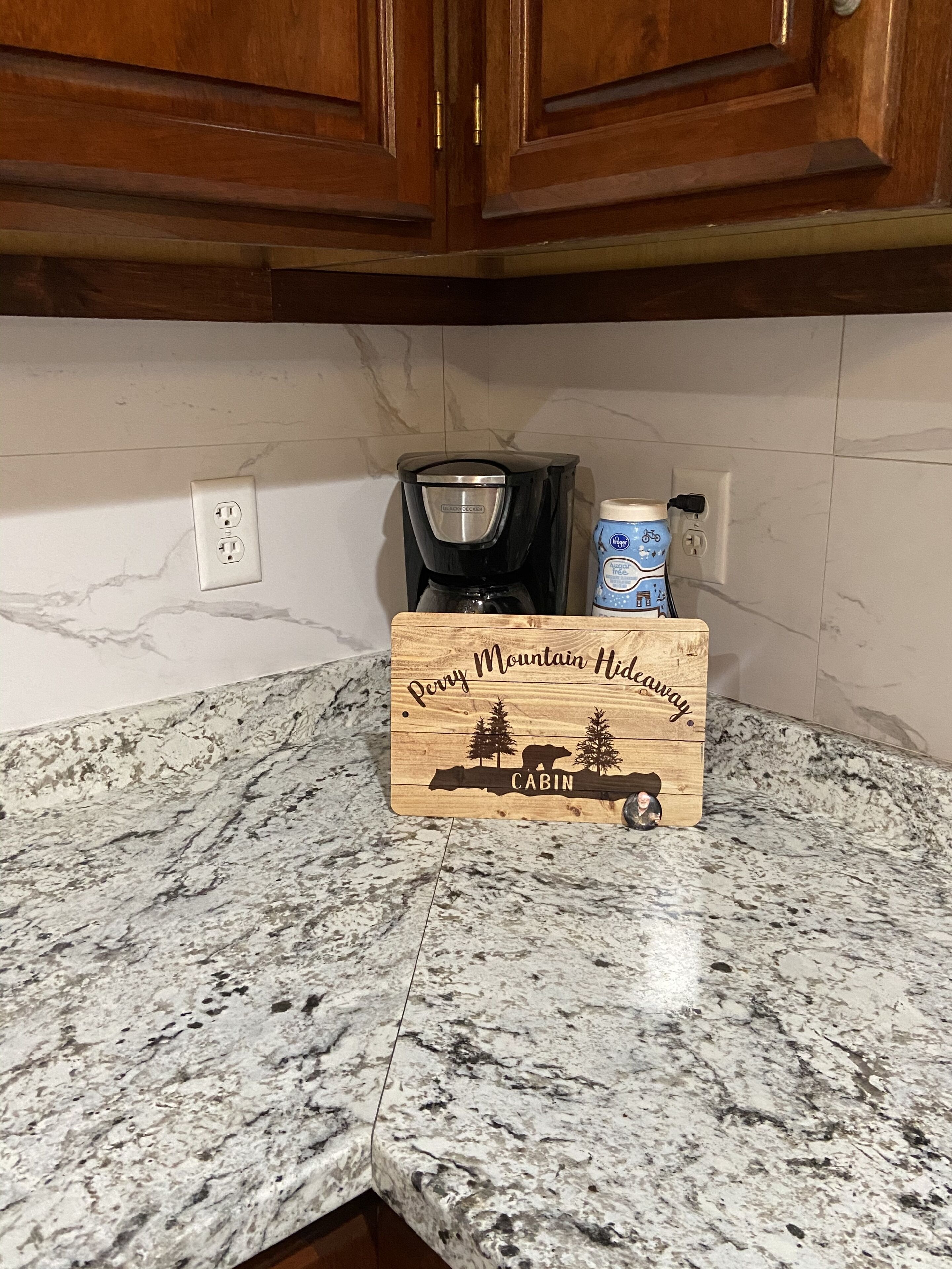 Una encimera de cocina con una cafetera, una taza de café y un letrero de madera que dice "Perry Mountain Hideaway Cabin".
