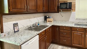 Una cocina con armarios de madera, encimera de granito, pileta de acero inoxidable, microondas y cafetera.