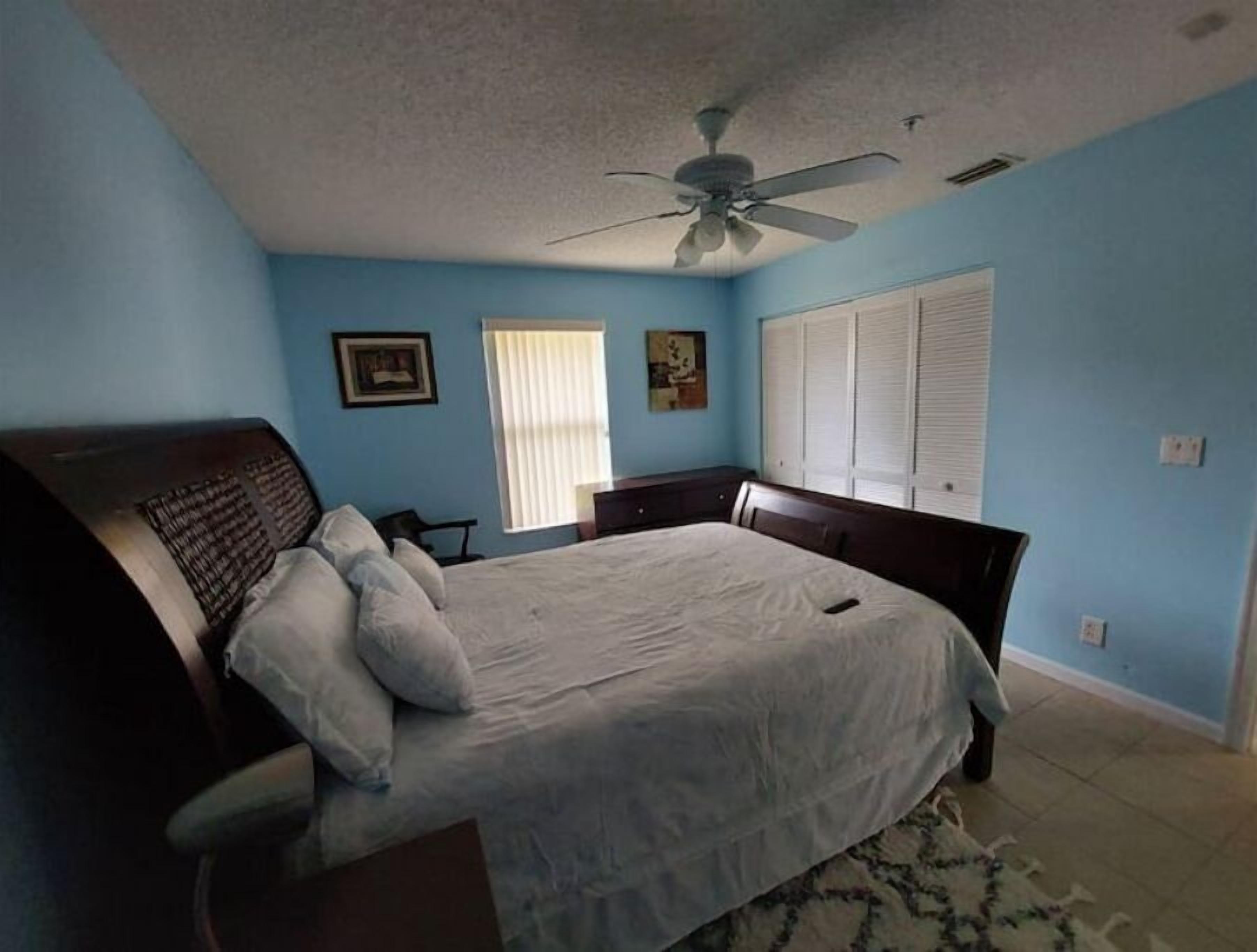 Ein Schlafzimmer mit einem Bett, einem Deckenventilator, einem Fenster mit Jalousien und einer Tür mit Einbauschrank.
