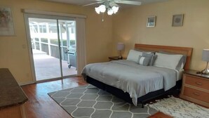 Une chambre à coucher comprenant un lit, des tables de chevet, un ventilateur de plafond et une vue sur l’extérieur, accessible par une porte-fenêtre coulissante.