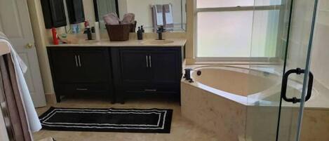 Un baño con bañera, cabina de ducha de vidrio y tocador con lavabo y espejo.