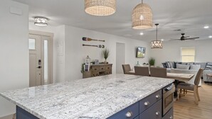 A modern kitchen with a granite island, pendant lighting, and a dining area with a wooden table and chairs. - Lake house retreat. (Inverness)