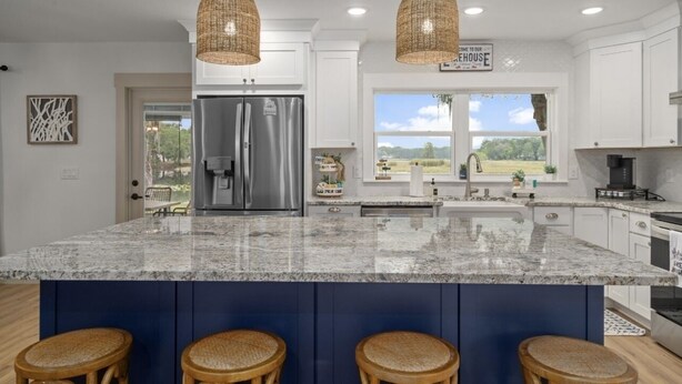 A modern kitchen with a large island, stainless steel appliances, wicker pendant lights, and a view of the outdoors. - Lake house retreat. (Inverness)