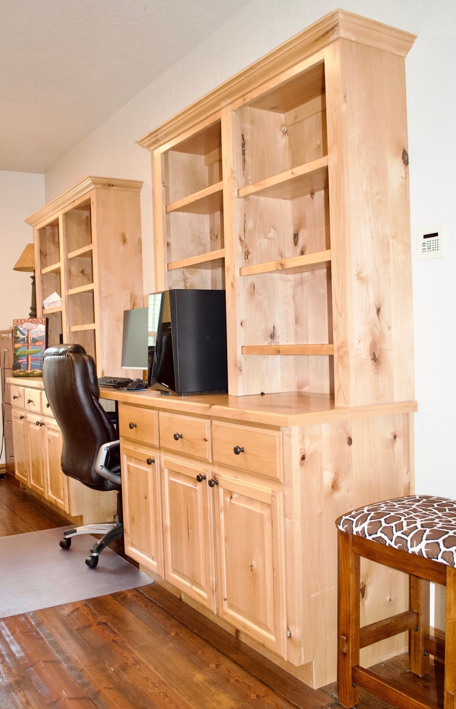 Quarto com uma escrivaninha de madeira, um computador e uma cadeira. Há uma estante com vários compartimentos.