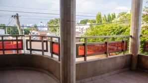 Un balcon doté d’une balustrade incurvée, une vue sur la rue et de la verdure en arrière-plan.