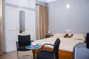 A hotel room with a bed, a small table with a chair, a nightstand, and a mirror. - Studio cosy et confortable (Lomé)