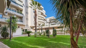 A multi-story hotel with balconies, a well-maintained lawn, and palm trees. - GuestHost - Grazia Attic Apartment with terrace (Trani)