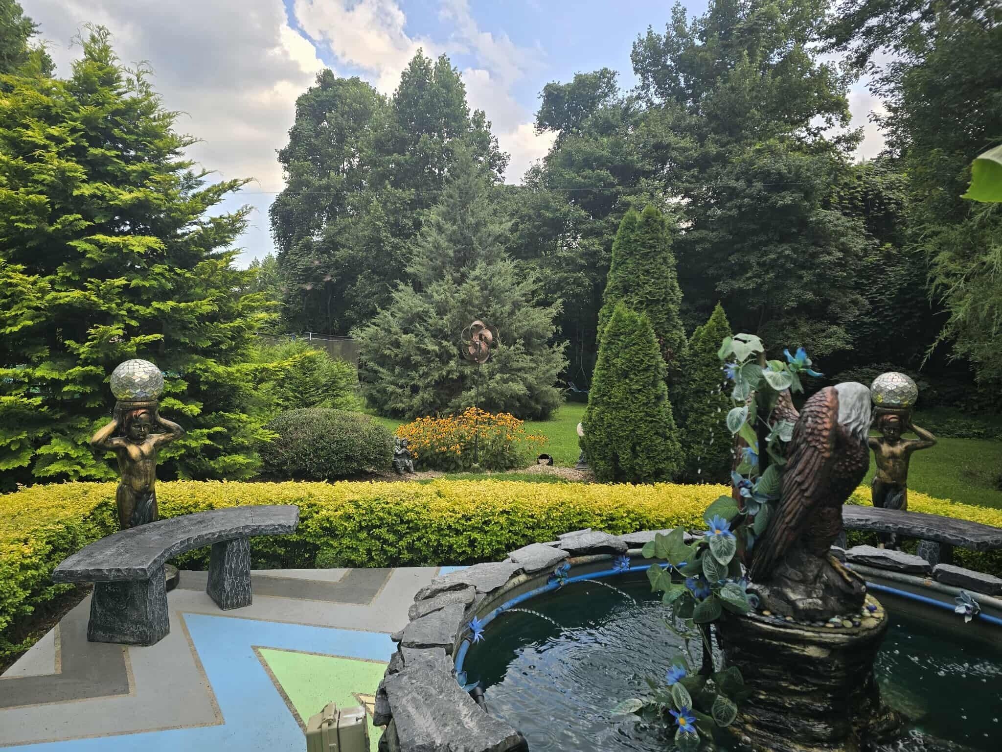 A garden with statues, a pond, and a variety of trees and shrubs.
