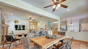 A spacious living room with a wooden dining table, comfortable seating, a fireplace, and a ceiling fan.