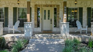 A building with a stone facade, a front door with glass panels, and two white Adirondack chairs on either side of a concrete path leading to the entrance.