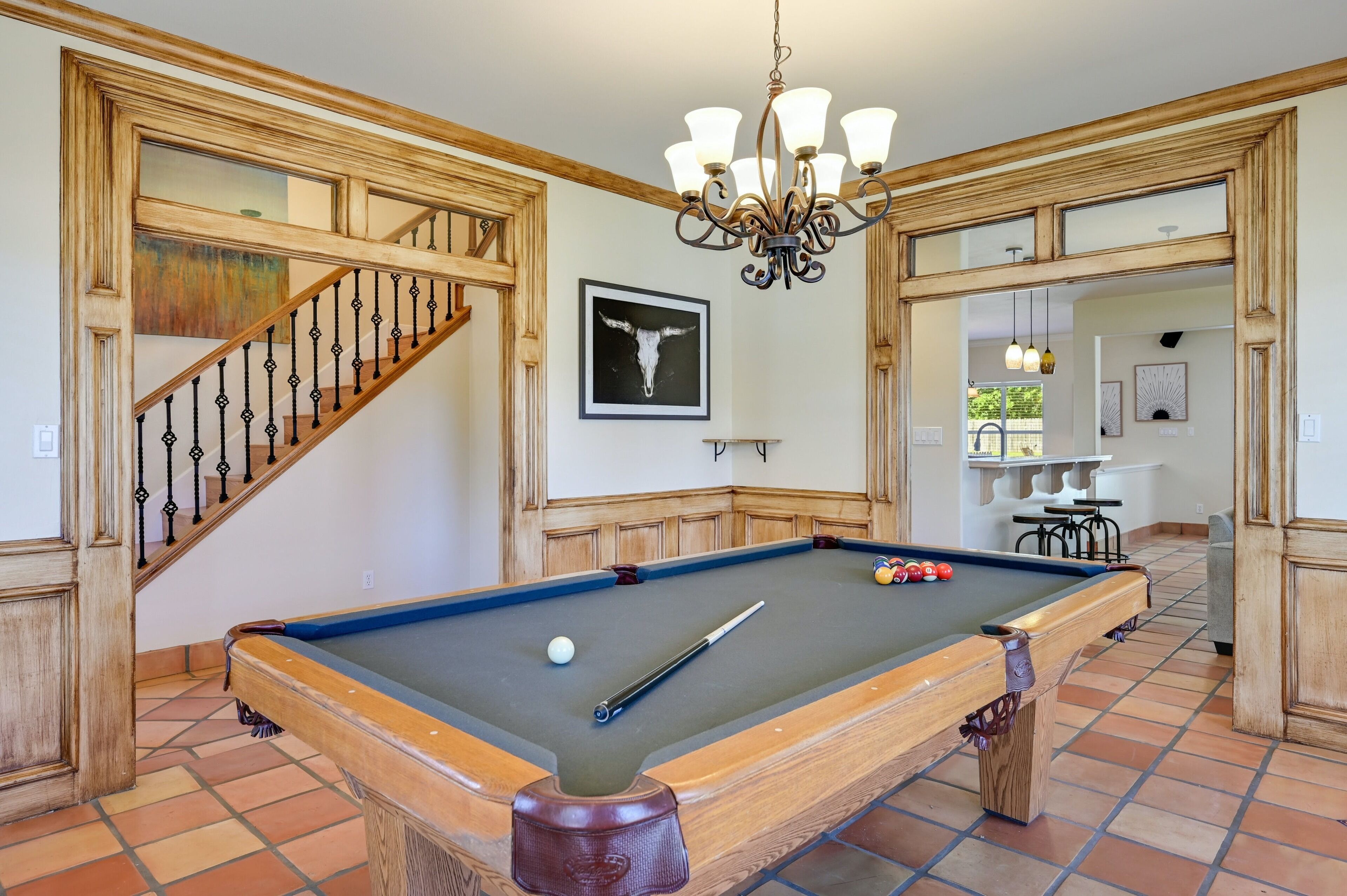 Une table de billard dans une pièce aux murs lambrissés et ornée d’un lustre.