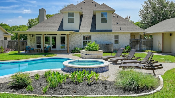A two-story house with a backyard featuring a swimming pool, a hot tub, and outdoor seating.