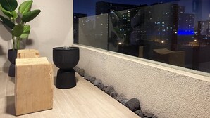 A modern balcony with a potted plant, a wooden block, and a black planter.