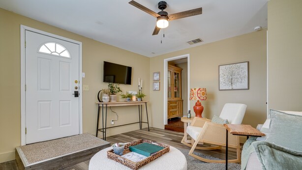 A living room with a white door, a ceiling fan, a TV, a wooden desk, a rocking chair, and a white couch.