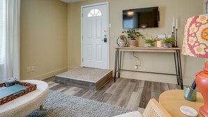 A living room with a sofa, a coffee table, a TV mounted on the wall, a door, and a small console table with decorative items.