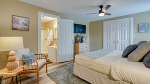 A bedroom with a bed, a chair, a desk, a dresser, and a door leading to a bathroom.