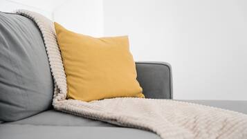 Un sofá gris con un cojín amarillo mostaza y una manta blanca.