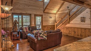 Ein Holzblockhaus-Interieur mit Kamin, Ledersofa und einer Treppe.